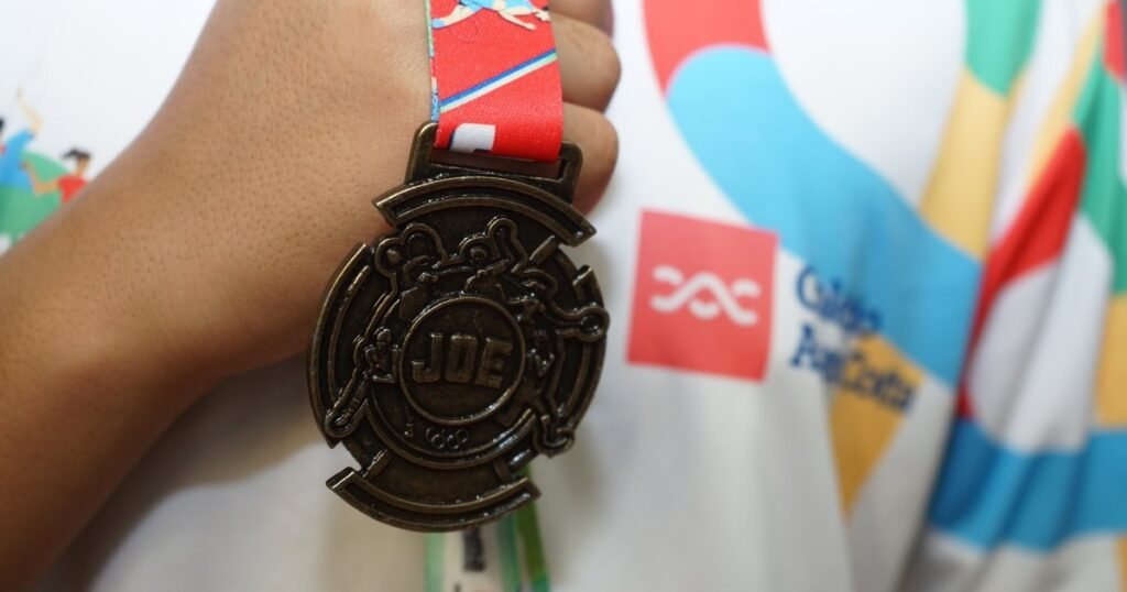 Medalha do JOE, os Jogos Olímpicos Estudantis, com a marca do Colégio Alceu Cotta ao fundo